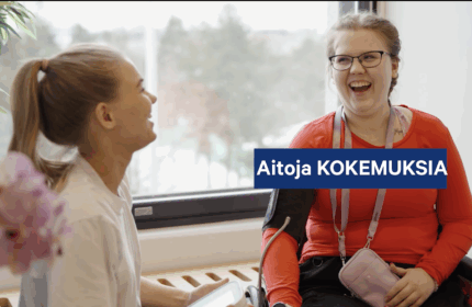 Kaksi naista juttelee iloisesti ikkunan edessä – toinen mittaa verenpainetta ja toinen istuu pyörätuolissa hymyillen. Kuvassa teksti: 'Aitoja KOKEMUKSIA.fi'.